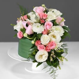 Pink and white floral arrangement in a green hatbox on a white stand