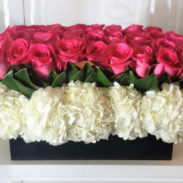 Pink roses arranged above white hydrangeas in a black rectangular box