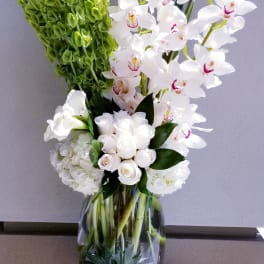 White orchids and roses arranged in a glass vase with green blooms