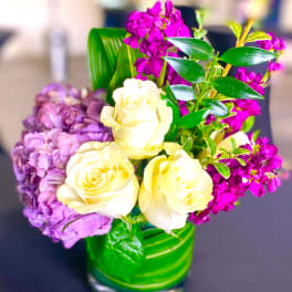 Cream roses and purple flowers arranged in a green glass vase