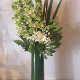 Tall green floral arrangement with orchids and calla lilies in a glass vase