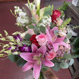 Handheld bouquet of pink lilies, roses, and white calla lilies