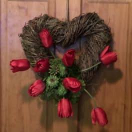 Heart-shaped twig wreath with red tulips on a wooden door