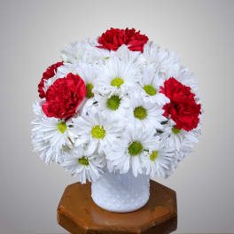 White daisies and red carnations arranged in a white vase