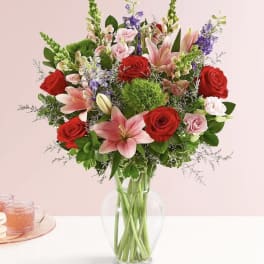 Bouquet of red roses, pink lilies, and purple flowers in a clear glass vase