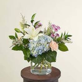 Mixed bouquet in a clear glass vase with white lily and blue hydrangea