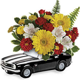 Yellow gerbera daisies, red carnations and white alstroemeria arranged in a black ceramic car container