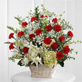 Tall white basket arrangement with red roses, white lilies, hydrangeas, and delicate white filler flowers