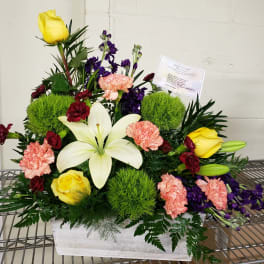 Mixed floral arrangement with yellow roses, white lilies, and pink carnations in a white container