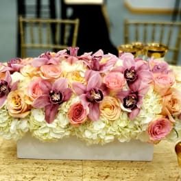 Pink orchids and roses arranged in a white rectangular vase