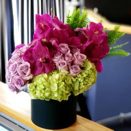 Pink orchids, lavender roses, and green hydrangeas in a black vase