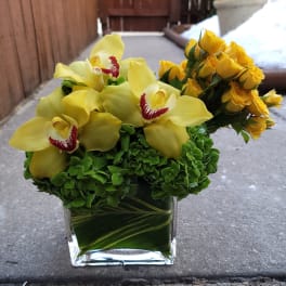 Yellow orchids and roses in a clear square vase