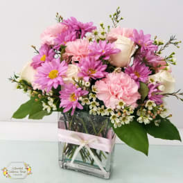 Pink and white bouquet in a clear square vase with a ribbon