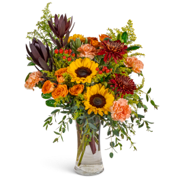 Bouquet of sunflowers, orange roses, and carnations in a clear glass vase