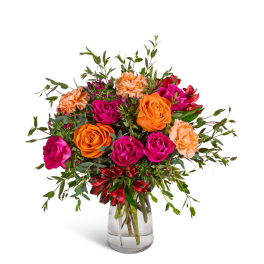 Bouquet of orange and pink roses with peach carnations in a clear glass vase.