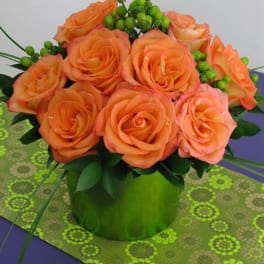 Compact arrangement of orange roses with green berries in a bright green cylinder vase.