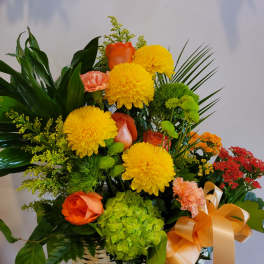 Basket arrangement with yellow mums, orange roses, and green hydrangea
