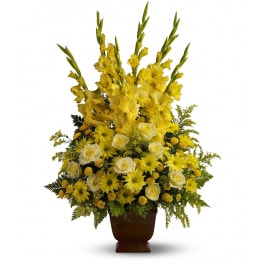 Tall yellow and white floral arrangement with gladiolus, roses, and daisies in a brown pedestal vase