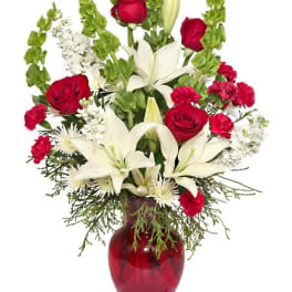 Tall arrangement of red roses, red carnations, and white lilies in a red glass vase
