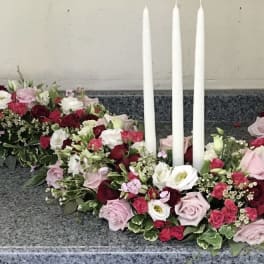 Floral wreath with red, pink, and white roses around three white candles