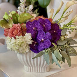 Bouquet of purple orchids, pink roses, and white hydrangea in a white vase