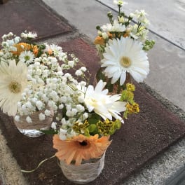 Small glass vases holding white daisies and orange gerbera daisies