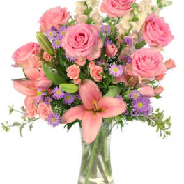 Pink roses, lilies, and purple asters arranged in a clear glass vase