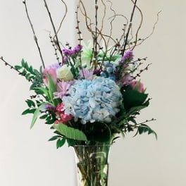Tall floral arrangement with blue hydrangea in a glass vase