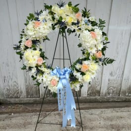 Heart-shaped floral wreath with white and peach flowers on a stand