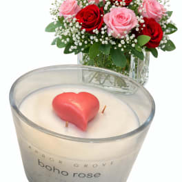 Pink and red roses in a glass vase beside a heart-shaped candle