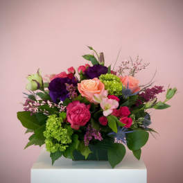 Mixed bouquet of pink, purple, and green flowers in a low rectangular container