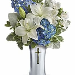 White lilies and blue flowers in a silver vase with a cross