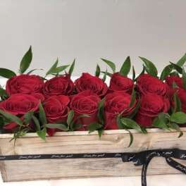 Red roses arranged in a wooden box with a black ribbon