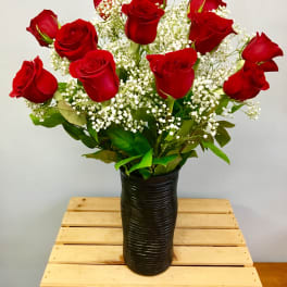 Red roses arranged in a black vase with white filler flowers