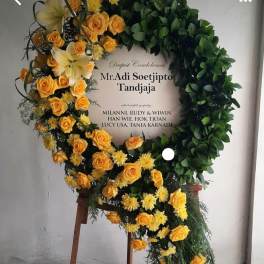 Large condolence wreath with yellow roses and white lilies on a stand