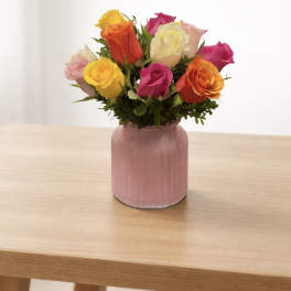 Mixed roses in a pink glass vase on a wooden table