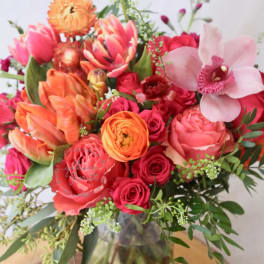 Mixed bouquet of pink, orange, and red flowers in a glass vase