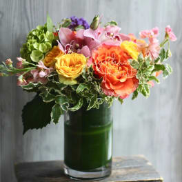 Mixed bouquet in a green glass vase with pink, orange, and yellow blooms