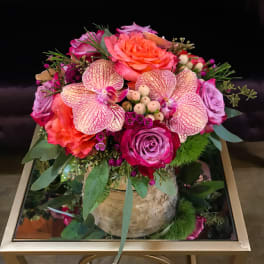 Pink and orange floral arrangement in a round container