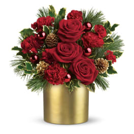 Round arrangement of red roses and carnations with evergreens in a gold cylinder vase.