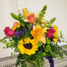 Mixed bouquet with sunflowers, roses, lilies, and snapdragons in a glass vase
