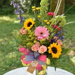 Mixed bouquet with sunflowers, pink gerberas, and roses in a glass vase