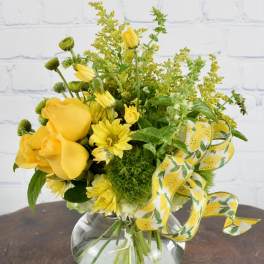 Yellow roses and daisies in a round glass vase with a yellow ribbon