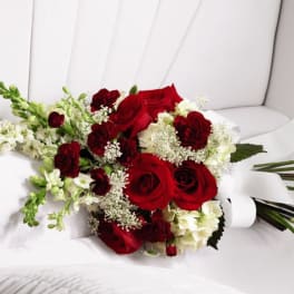 Hand-tied bouquet of red roses and white flowers with a white ribbon on a white cushioned surface