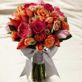 Hand-tied bouquet of orange, coral, and pink roses with tulips, wrapped in white satin ribbon and bow