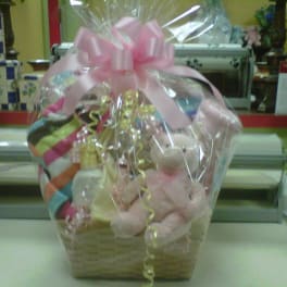 Gift basket wrapped in cellophane with pink bow, teddy bear, and baby items on a counter