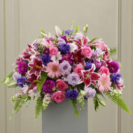 Large pink and purple flower arrangement with lilies, roses, and gerbera daisies on a gray pedestal stand