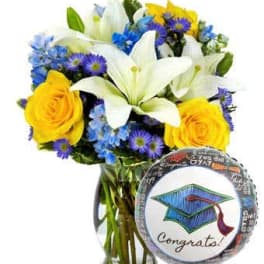 Bouquet of white lilies, yellow roses, and blue-purple flowers in a glass vase with a graduation balloon