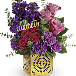 Purple and pink flower arrangement in a gold vase with a "celebrate" sign