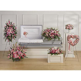 Funeral set with pink floral sprays, casket spray, wreath, and bouquet around an open silver casket.